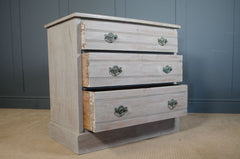 Wooden dresser with three drawers against a gray wall.