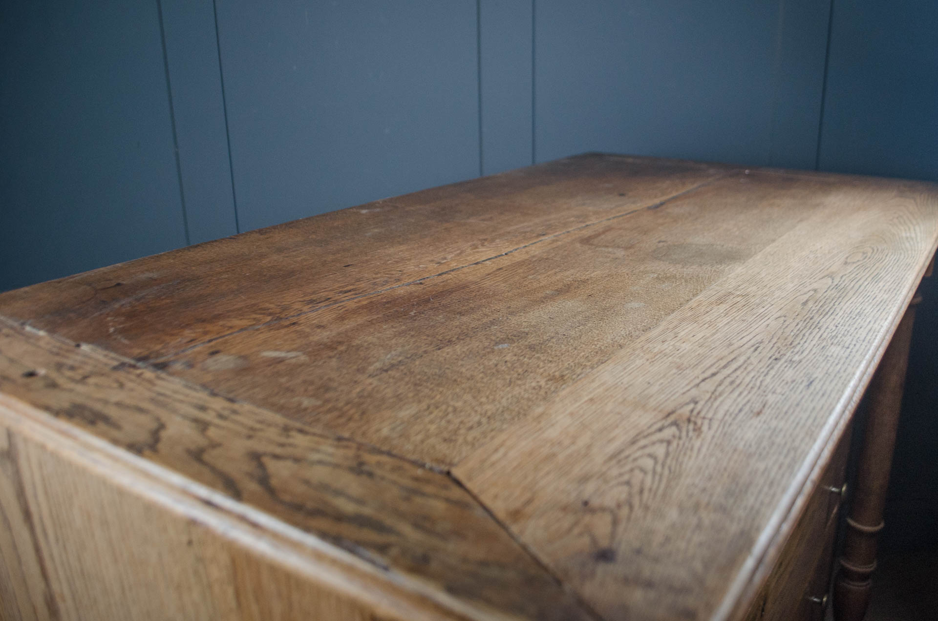 
Close-up of a rustic wooden table top with visible grain and wear, set against a dark blue paneled wall.