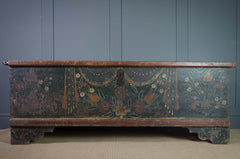 Antique hand painted wooden chest against a blue panelled wall with sisal carpet