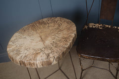 Round wooden stool with a textured surface next to a dark metal chair against a blue wall.