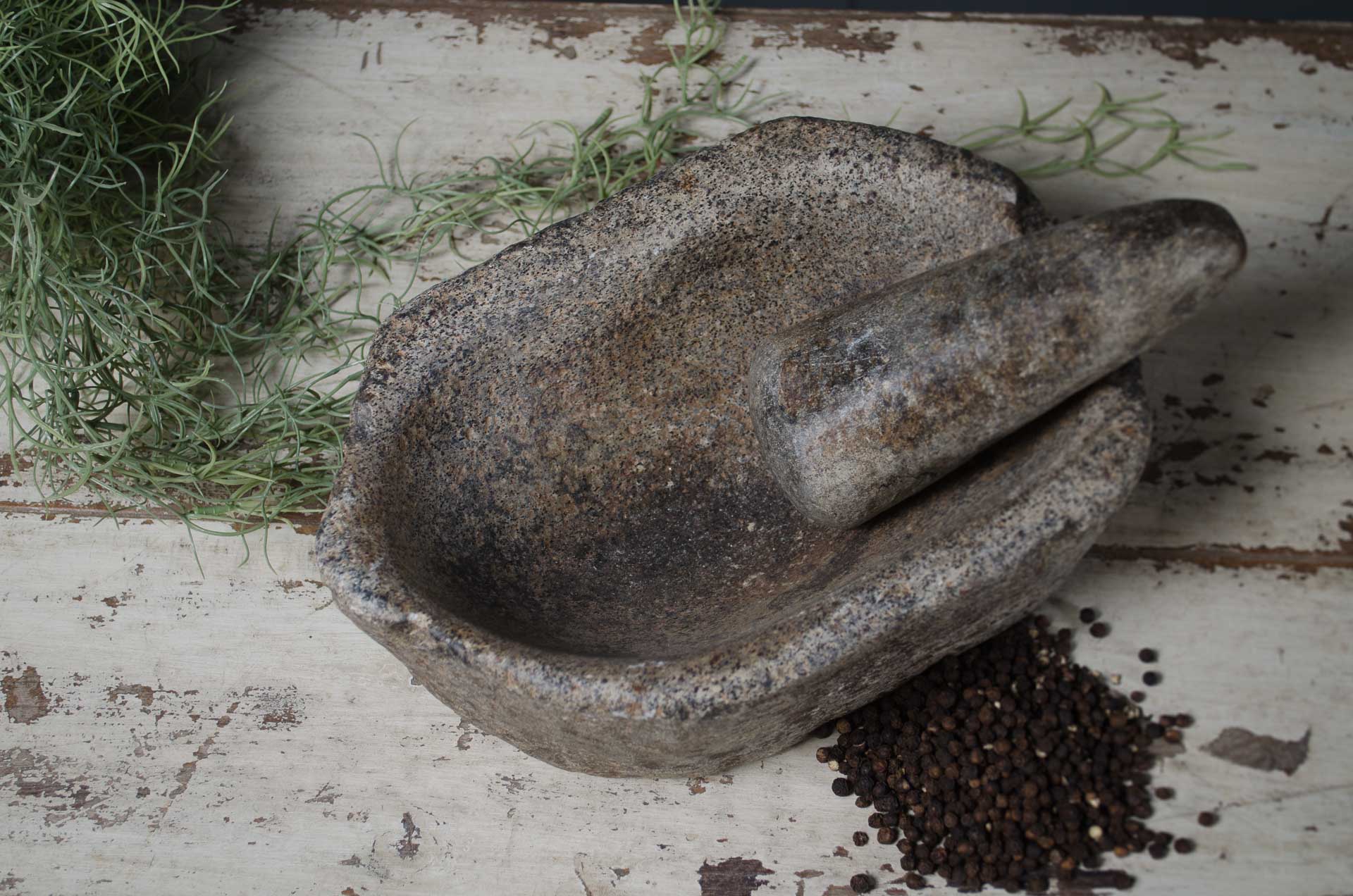 Stone mortar and pestle with herbs and peppercorns on a rustic wooden surface