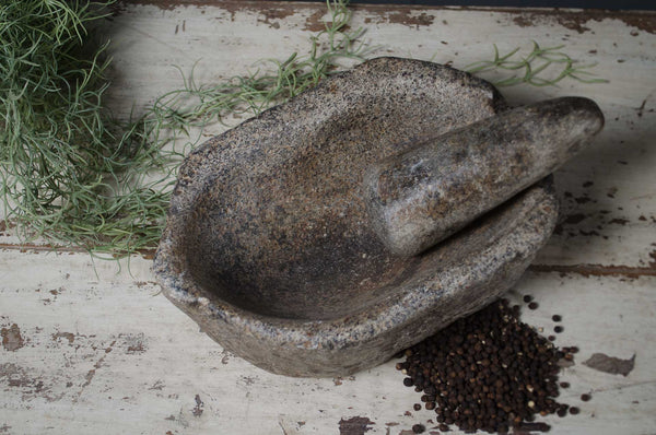 Stone mortar and pestle with herbs and peppercorns on a rustic wooden surface