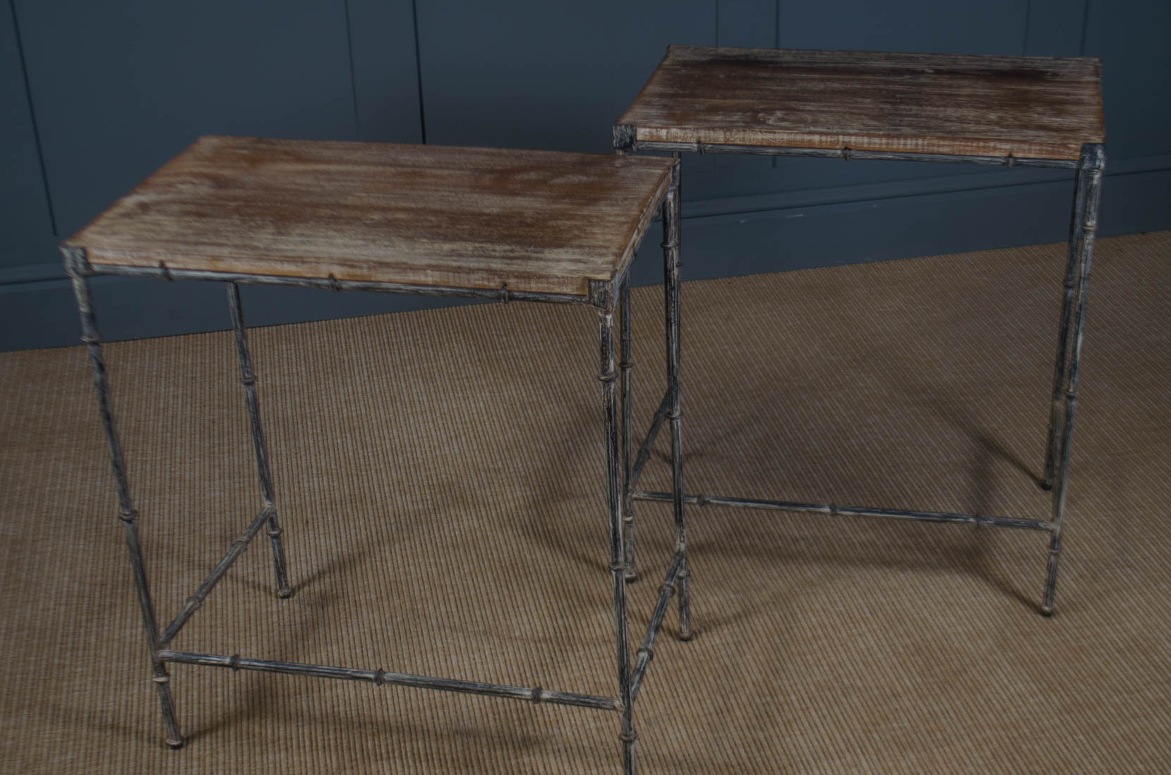 
Two rustic wooden tables with metal frames on a textured floor against a blue wall.