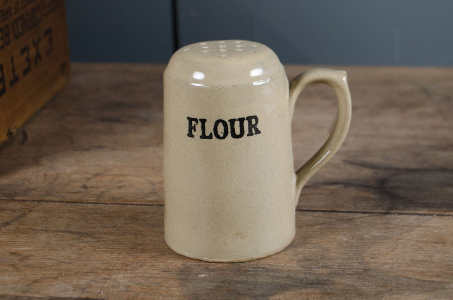 
Beige ceramic flour container with 'FLOUR' text on a wooden surface.
