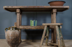 Vintage wooden table with a stool and rustic jars against a blue wall.