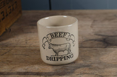 Ceramic container labeled 'Beef Dripping' on a wooden surface with a blue wall in the background.