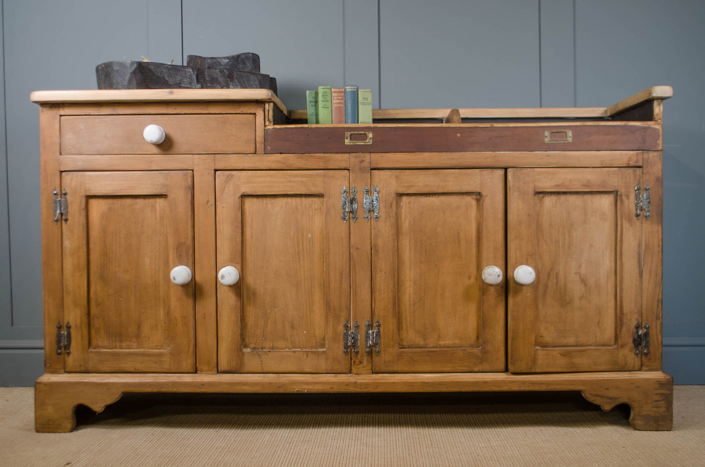 A vintage wooden sideboard cabinet with four doors, a single drawer, and a dark brown leather top, shown against a gray paneled wall.