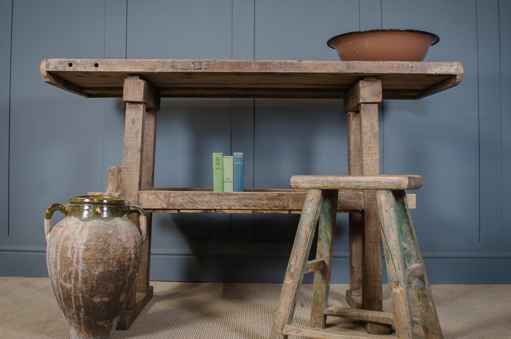 Vintage wooden table with a rustic jar and books against a blue wall.