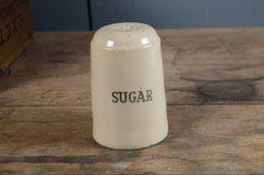 Vintage-style ceramic sugar container on a wooden surface with a blue wall in the background.