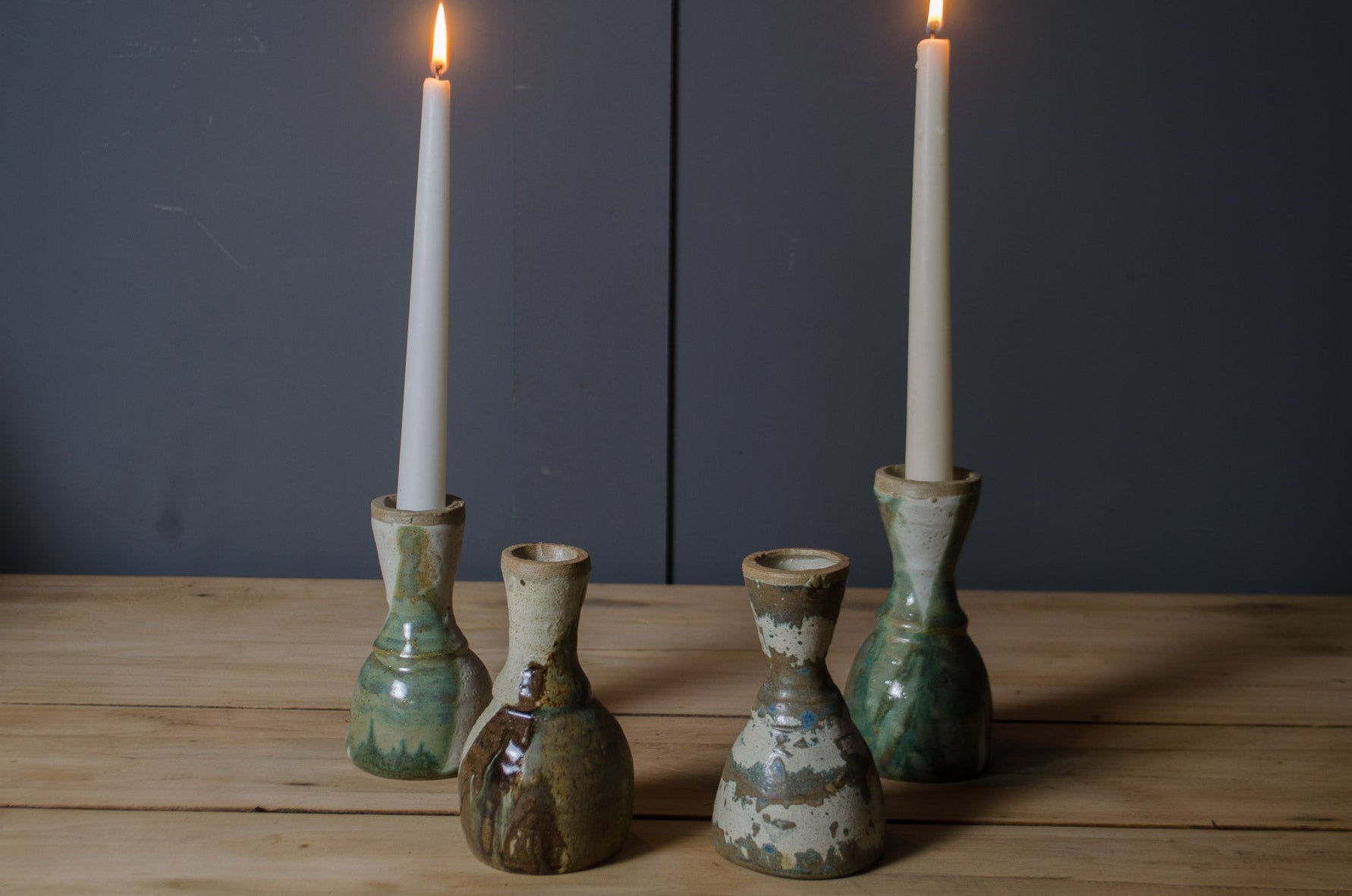Set of five ceramic candle holders with lit candles on a wooden surface against a dark background