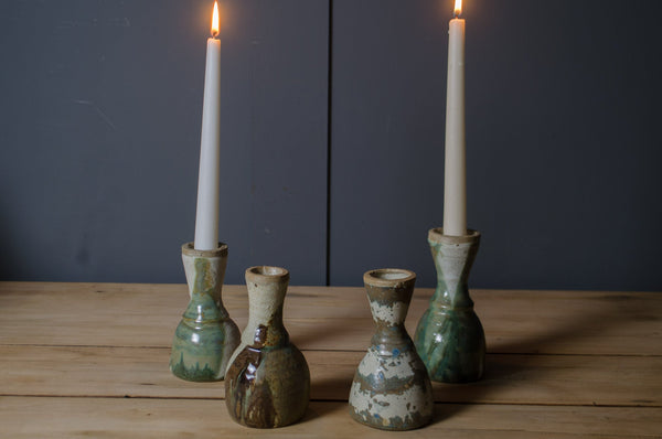 Set of five ceramic candle holders with lit candles on a wooden surface against a dark background