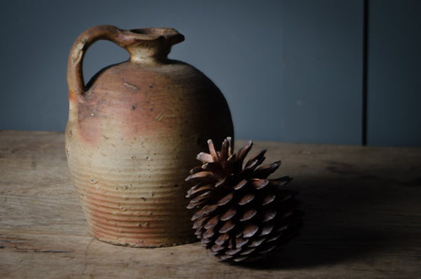 Stoneware jar and pine cone on a wooden surface with a dark background. french oil jug