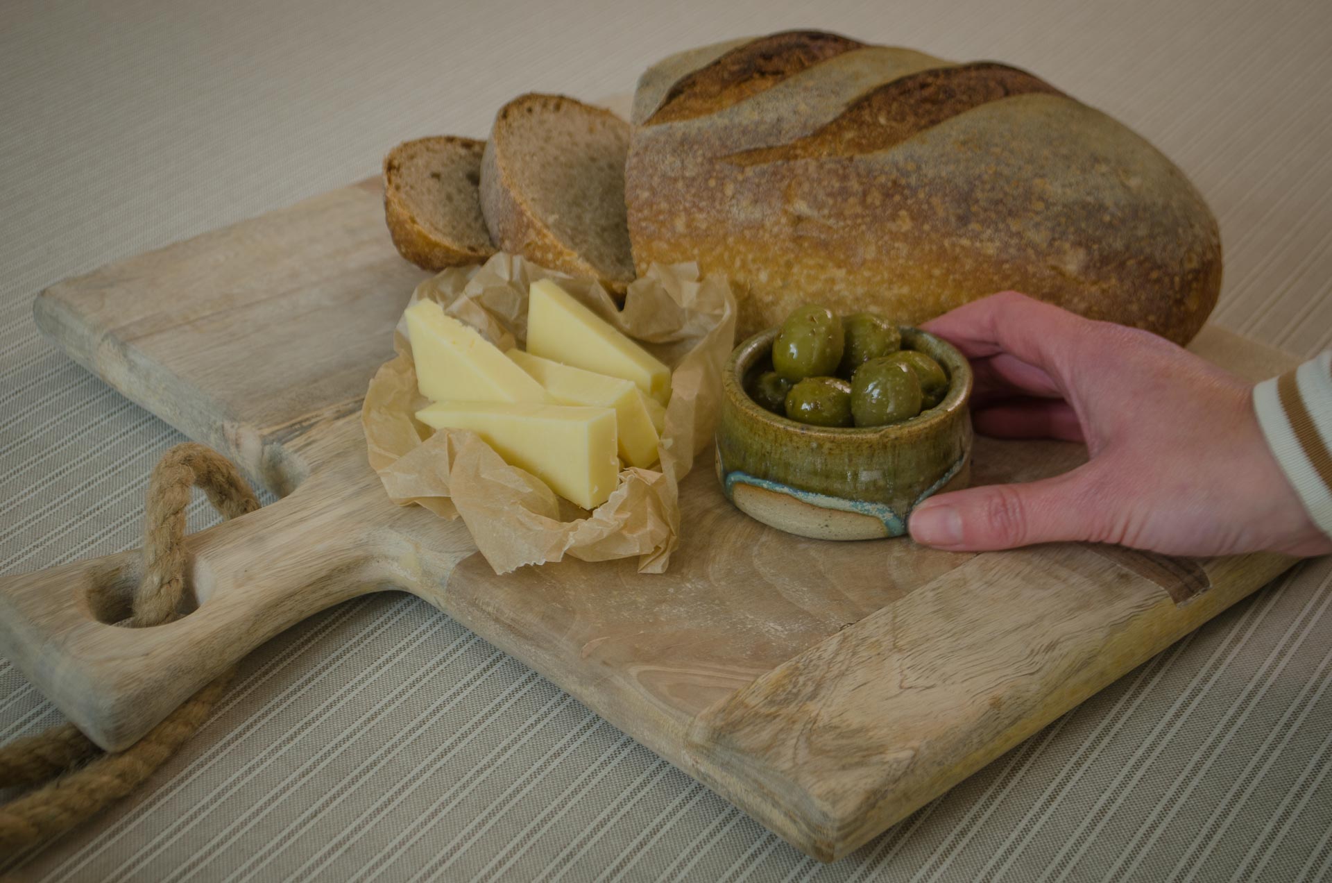 Rustic mango wood cheese board with olives, butter and sourdough bread