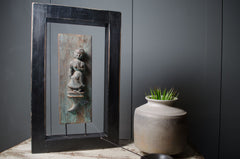 Decorative indian carved wall art with a black frame on a dark gray wall.