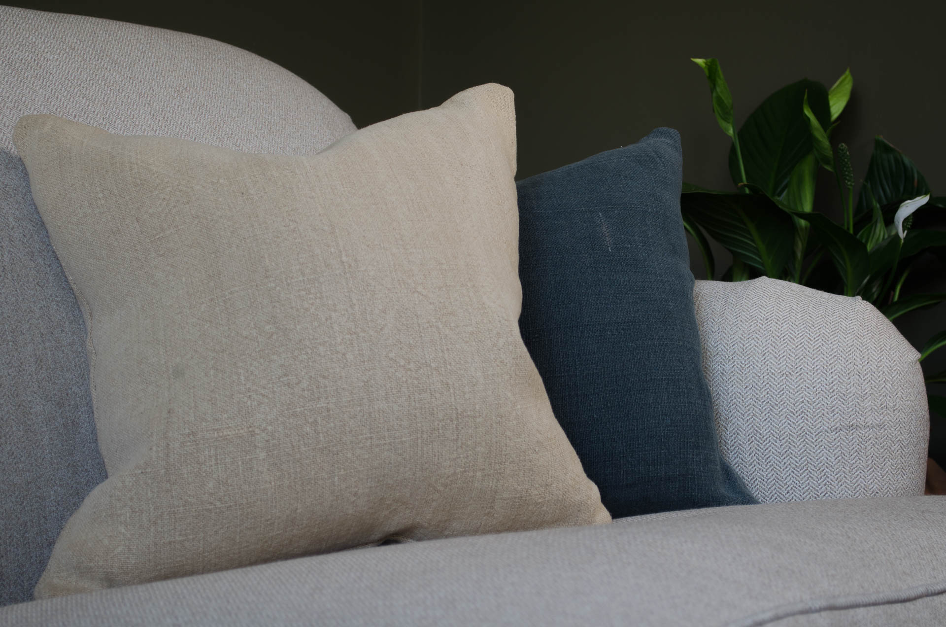 Beige and blue natural linen hempcushions on a grey sofa with a plant in the background