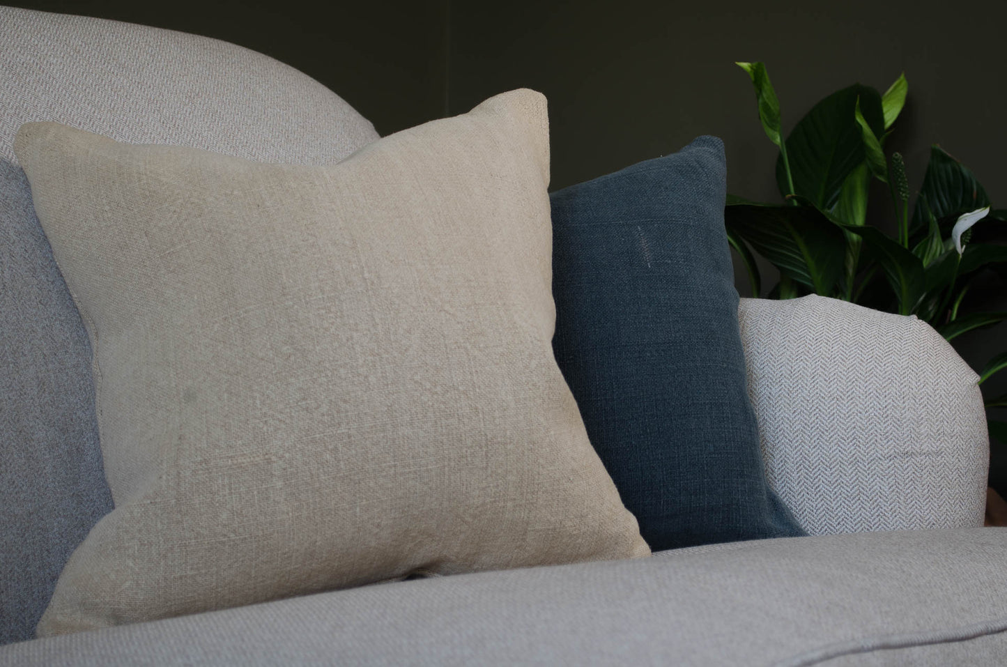 Beige and blue natural linen hempcushions on a grey sofa with a plant in the background