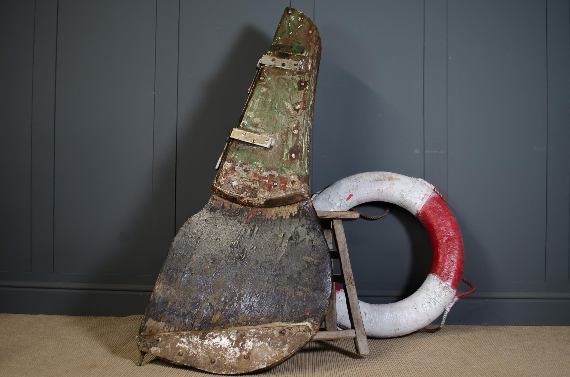 Rustic ships rudder with a life preserver against a gray wall.