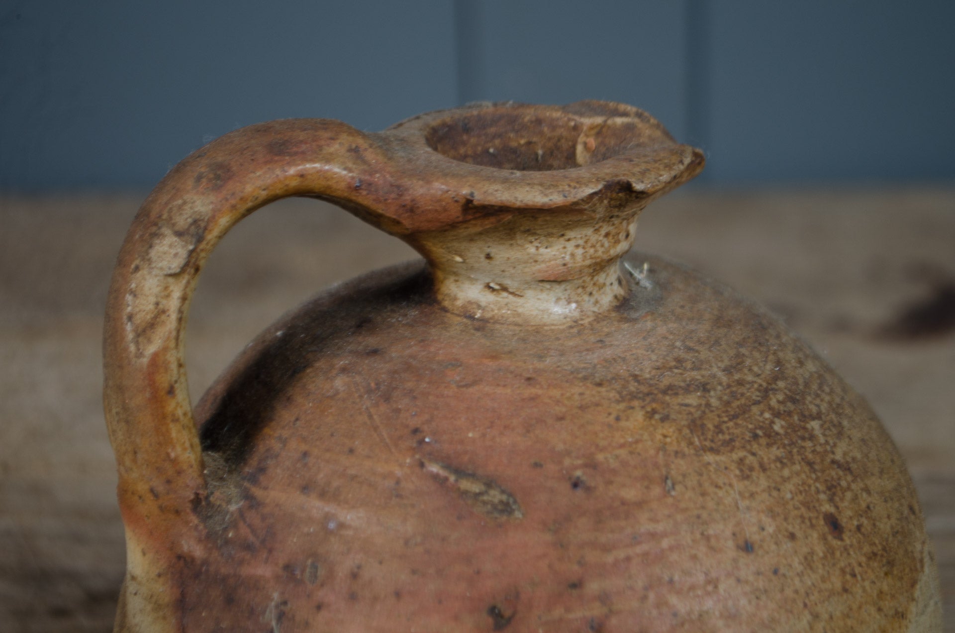 Rustic ceramic jar with a worn handle against a blurred background