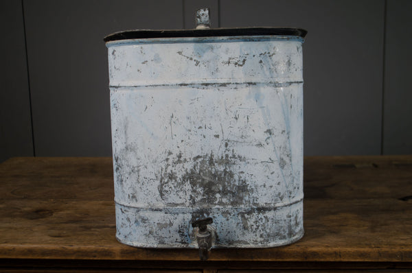 Vintage metal water dispenser with a rustic appearance on a wooden surface.