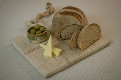Loaf of bread with slices on a wooden board with olives and cheese.