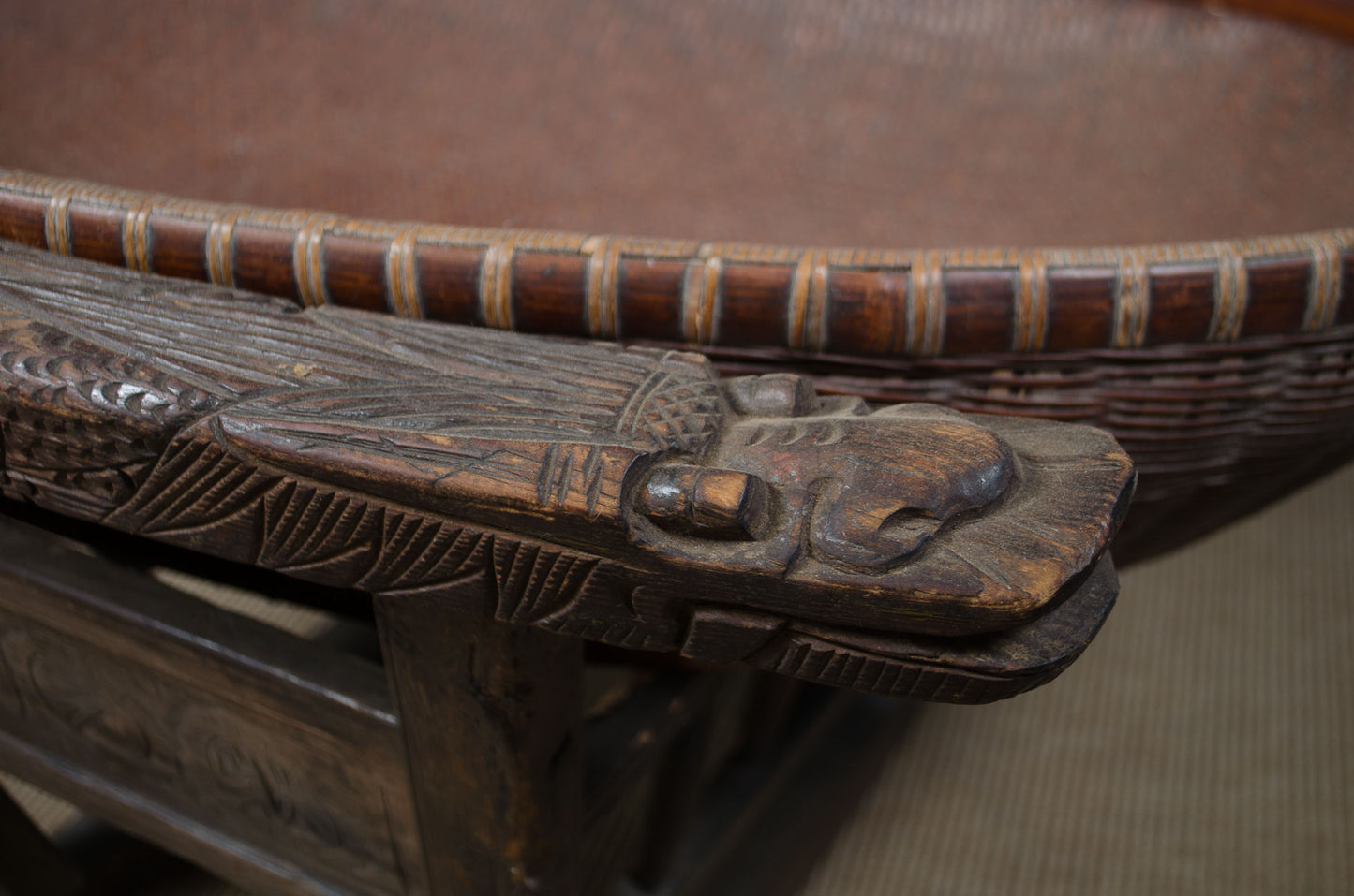 Close-up of a carved wooden table corner with a detailed dragon head topper and a woven basket or tray rim in the background.