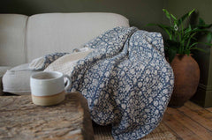 Floral-patterned blue blanket draped over a sofa with a cup on a wooden table.