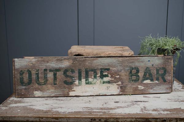 Wooden sign with 'OUTSIDE BAR' text on a rustic surface against a dark wall.