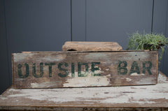 Wooden sign with 'OUTSIDE BAR' text on a rustic surface against a dark wall.