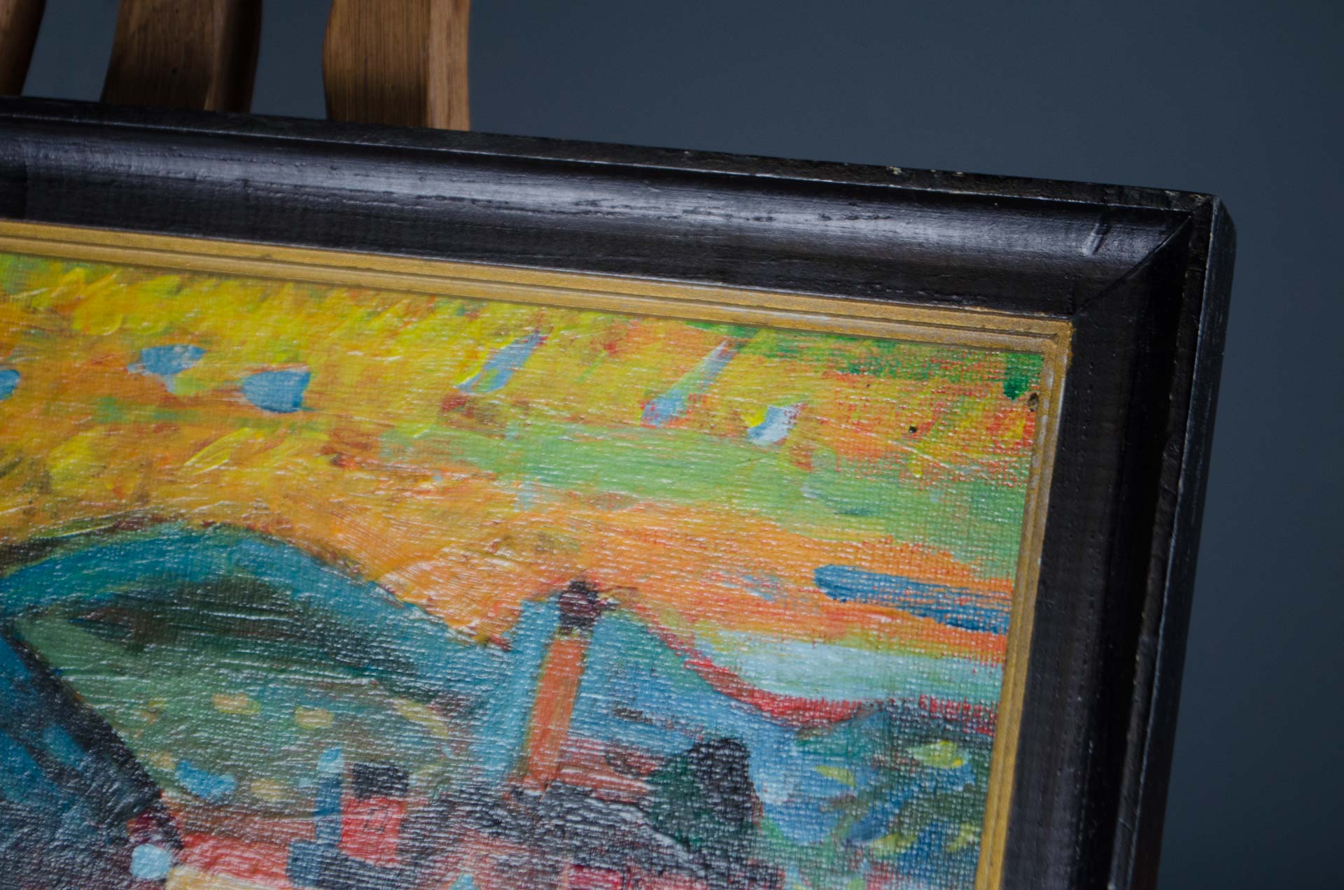 
A close-up of a framed painting on an easel, showing a colorful abstract landscape with yellow, orange, green, and blue brushstrokes inside a thick black frame.