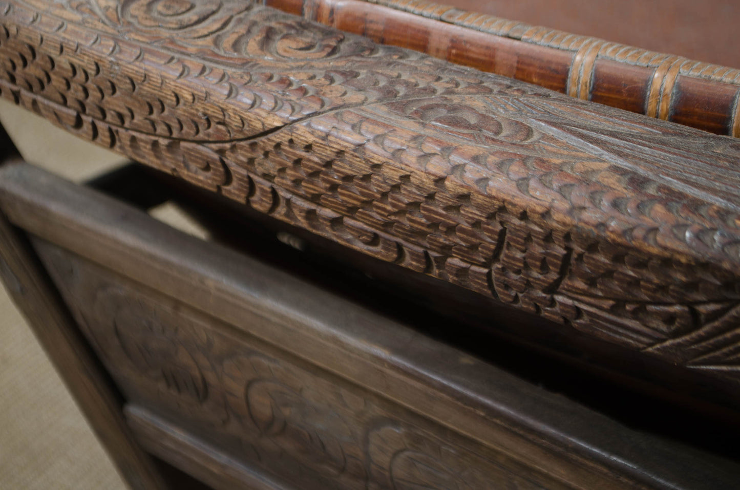 Close-up of an intricately carved dark brown wooden furniture piece, showing detailed hand-carved patterns on the armrest and side panel.