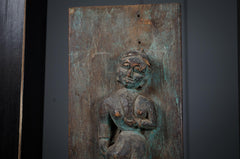 Bronze plaque with a seated figure on a dark background