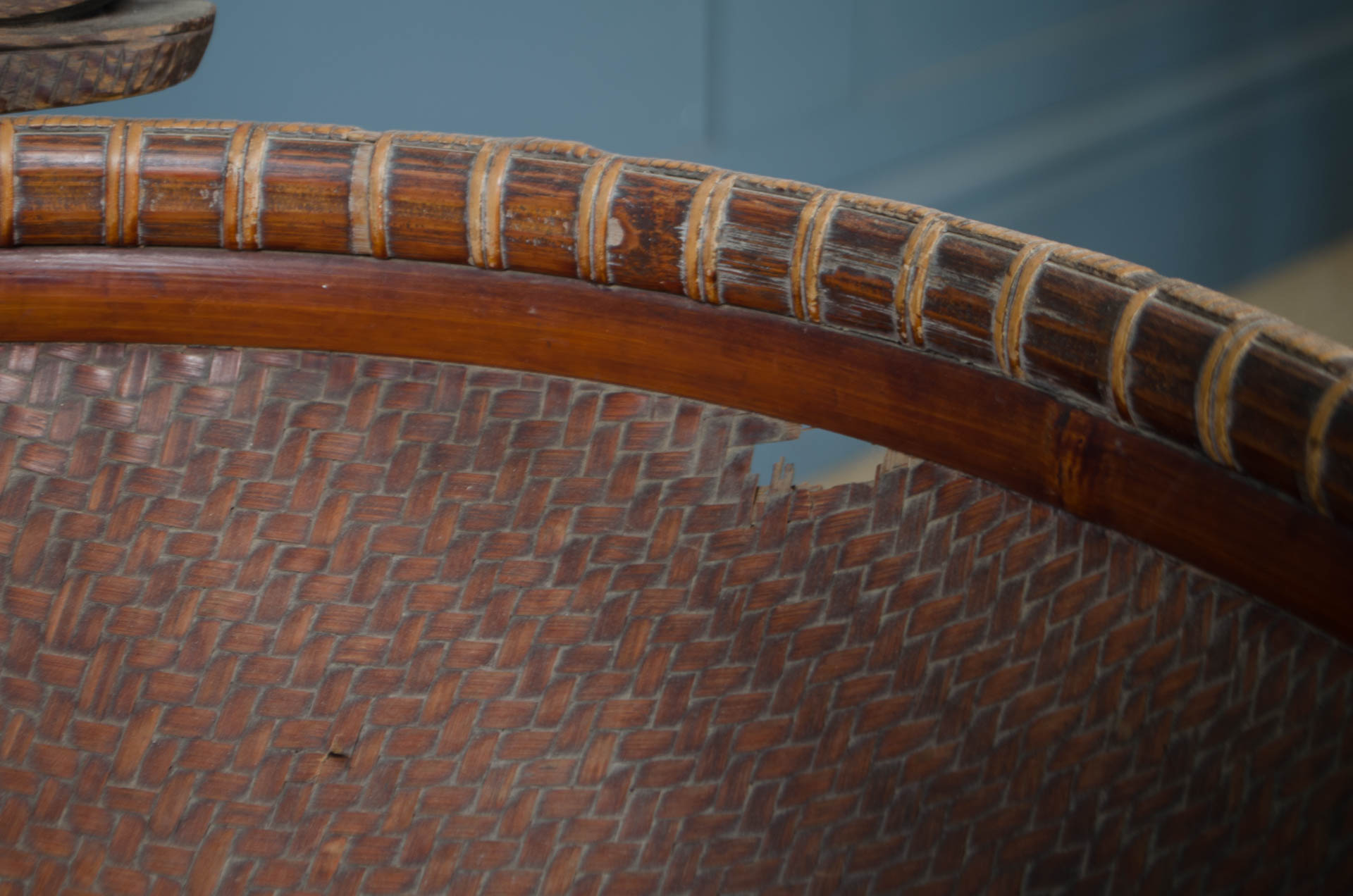 
Close-up of a woven rattan or wicker chair back with a curved brown wooden armrest and natural fiber binding.