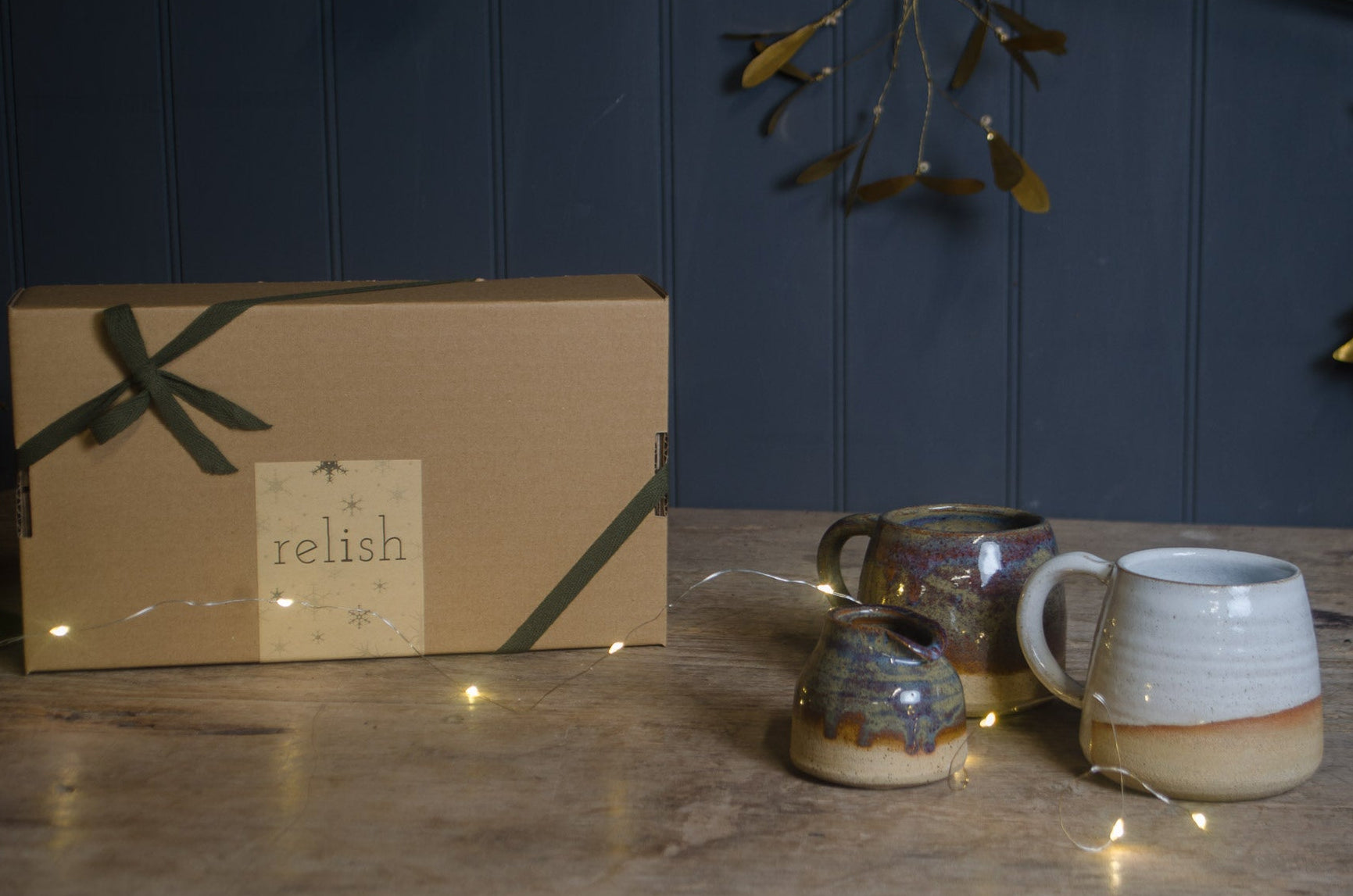 Two hand made ceramic mugs on a wooden surface with a gift box labeled 'relish' in the background.