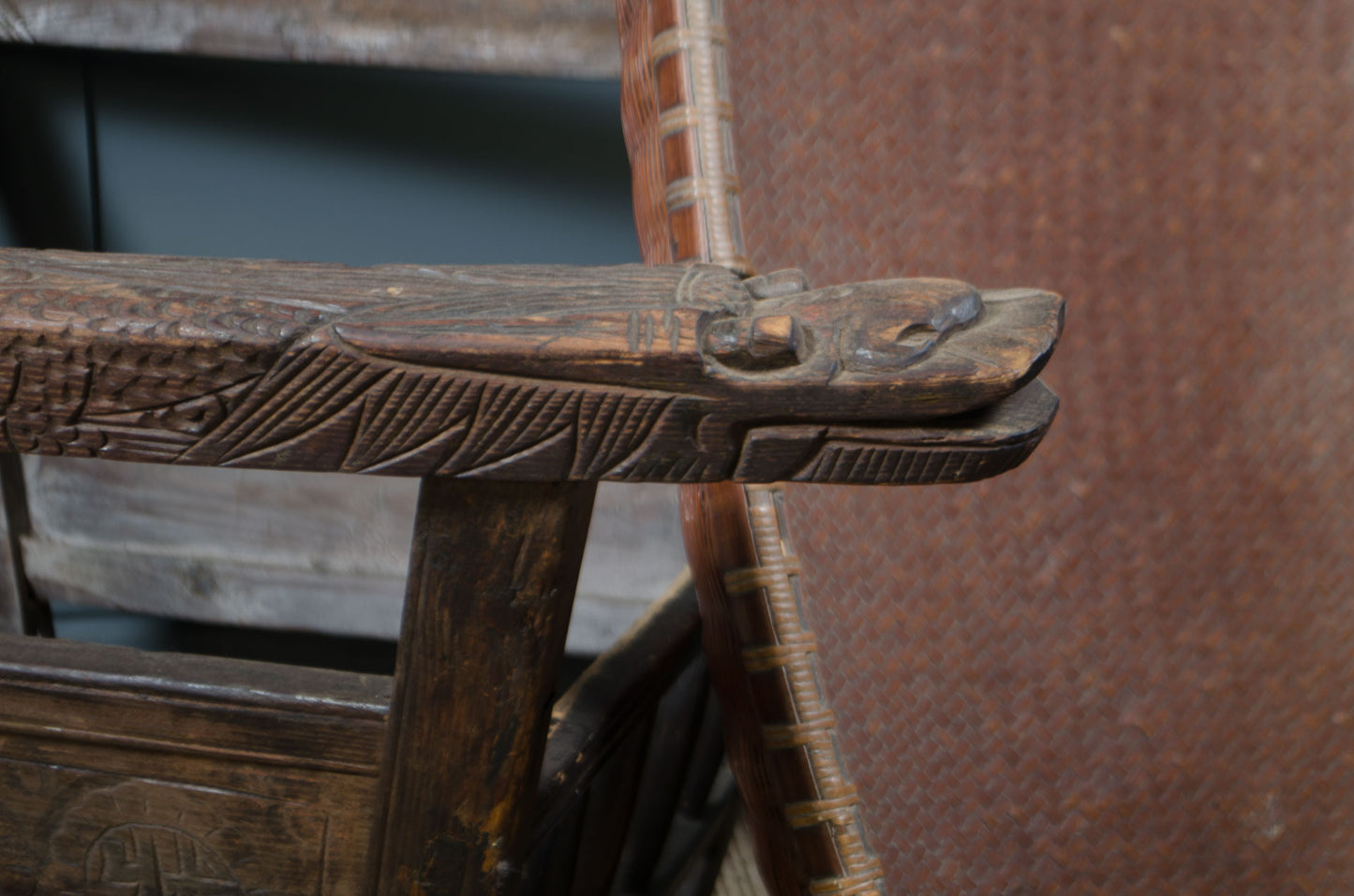 Close-up of a dark carved japanese rocking wooden chair arm with a detailed animal head carving, showing the texture and craftsmanship of the wood.