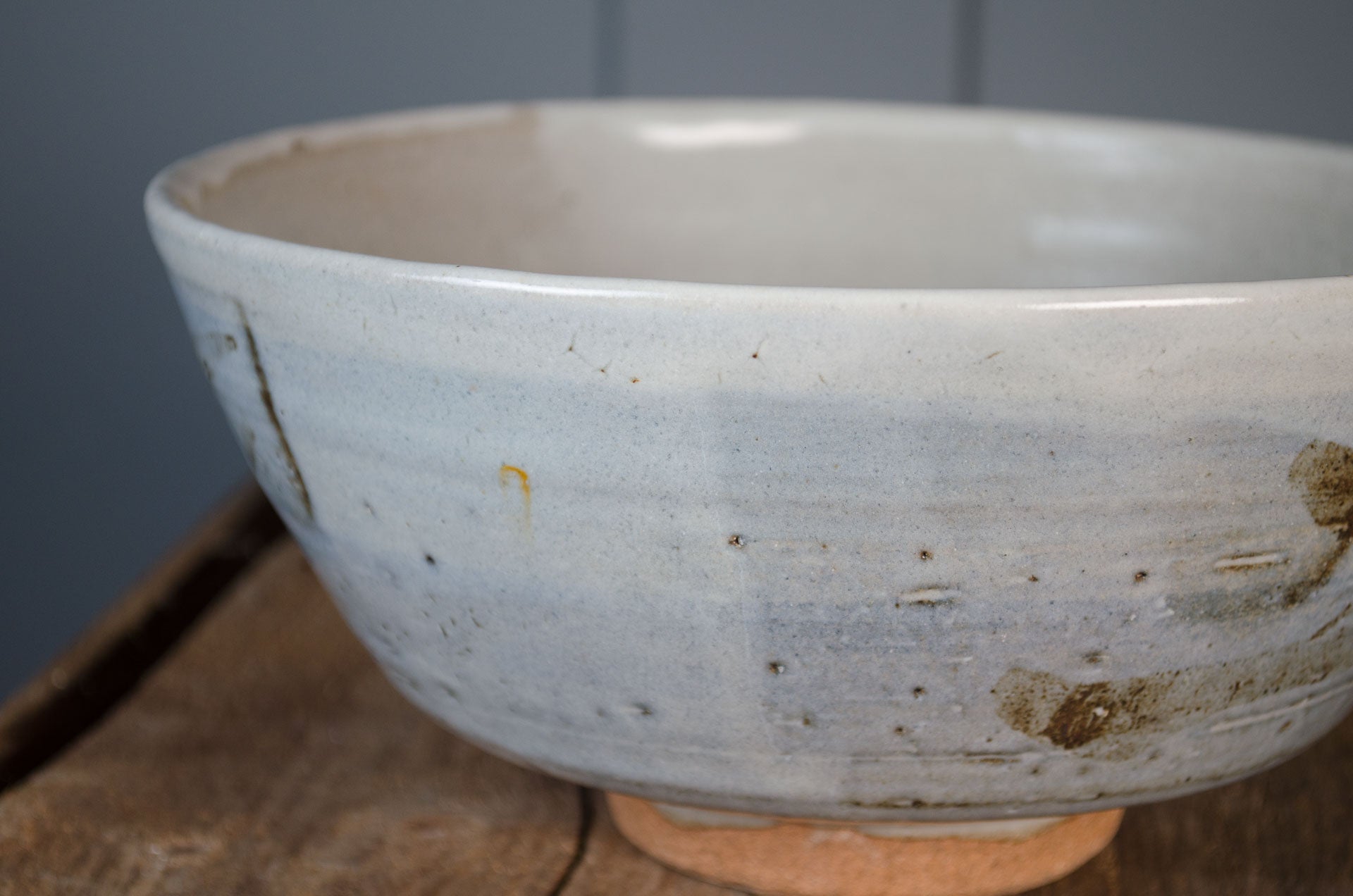 Ceramic bowl with a speckled glaze on a wooden surface against a gray wall believed to be by Leach St ives