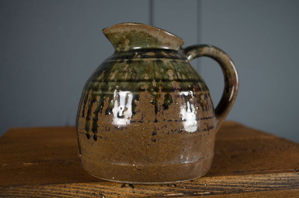 Stoneware pitcher with green and brown glaze on a wooden surface