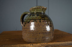 Stoneware pitcher with a textured surface on a wooden surface against a gray background