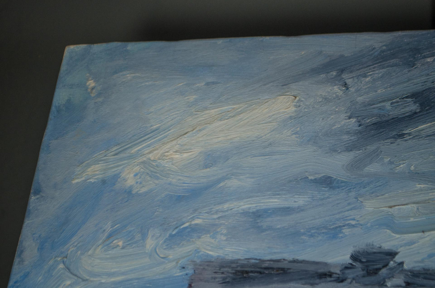 An abstract canvas painting featuring textured brushstrokes of light blue, white, and gray paint, shown at an angle against a dark background.