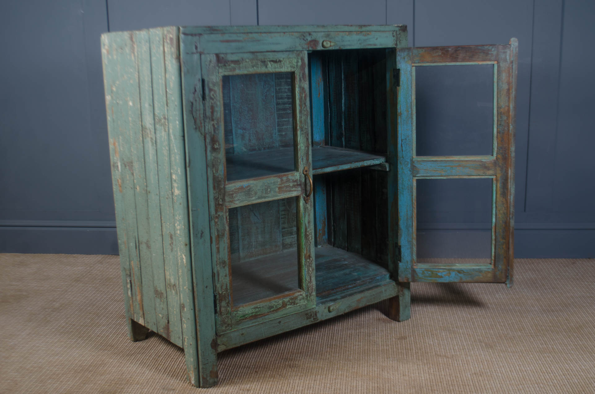 
Vintage-style wooden cabinet with a distressed blue finish against a gray wall.
