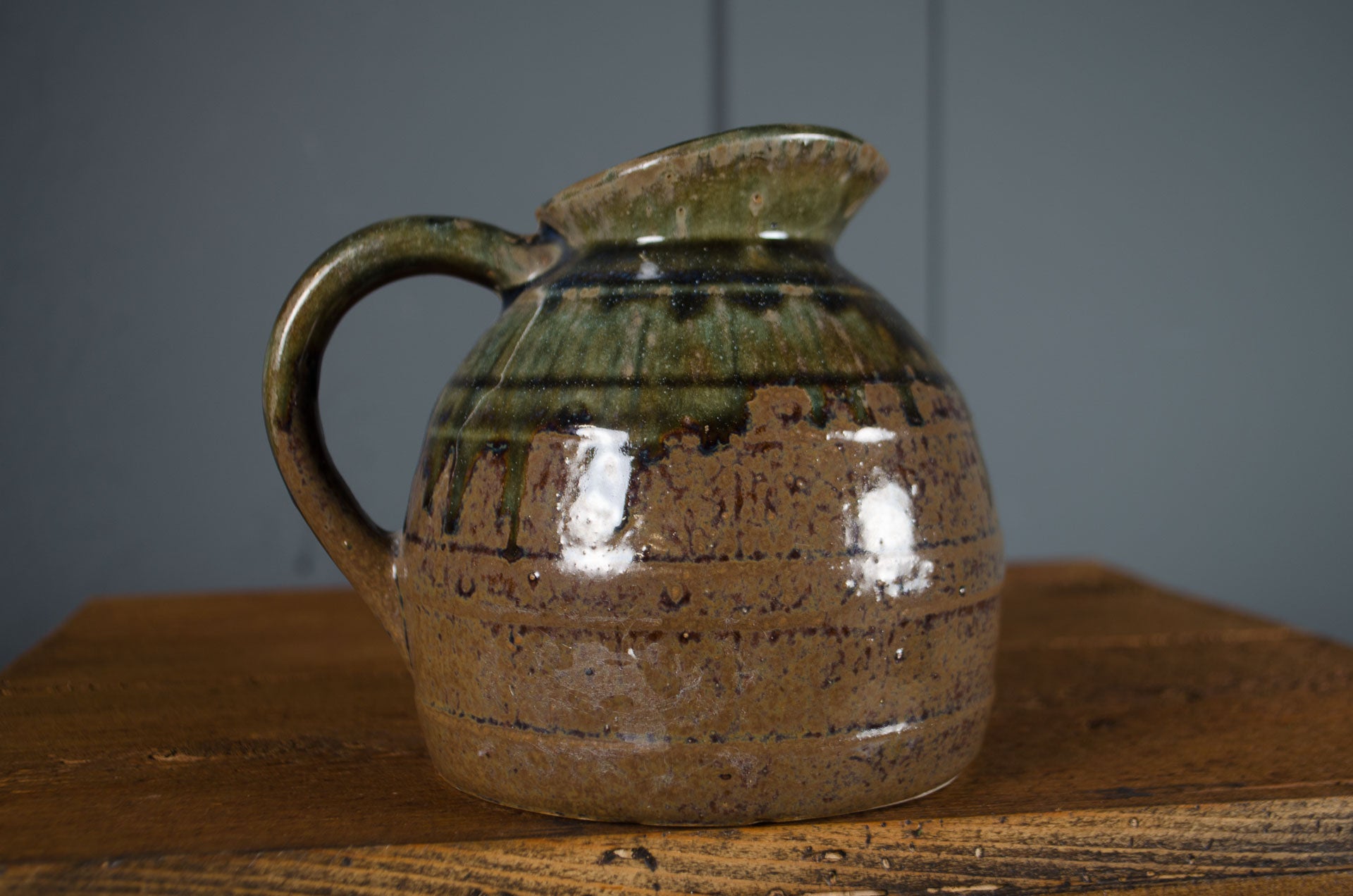 Ceramic pitcher with green and brown glaze on a wooden surface