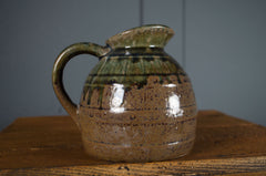Ceramic pitcher with green and brown glaze on a wooden surface