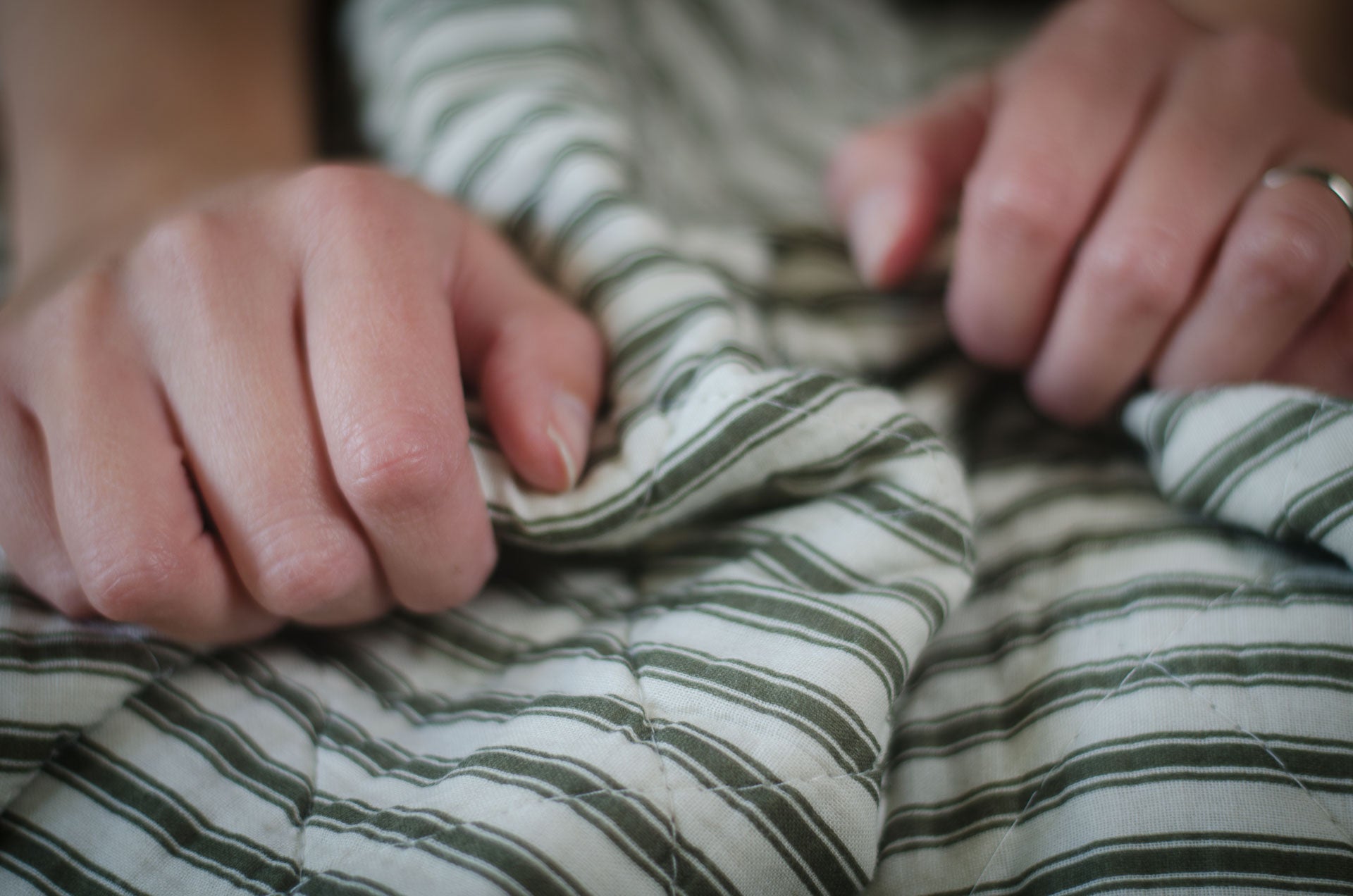 Close-up of hands holding a cosy quilted green stripe blanket