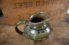 Green ceramic pitcher on a wooden surface with a background of 'Ground Beef' packaging.