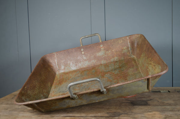 Rust industrial metal tray with handles on a wooden surface against a gray wall.