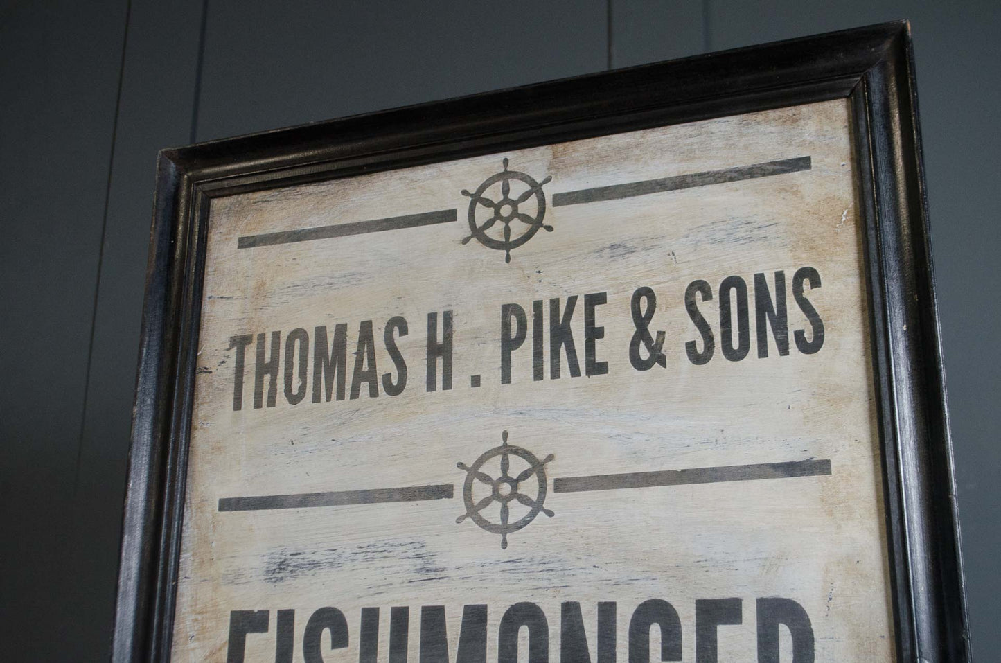 A framed rustic wooden sign with a distressed cream background, black ship wheel graphics, and the text 'THOMAS H. PIKE & SONS' and 'FISHMONGER'.