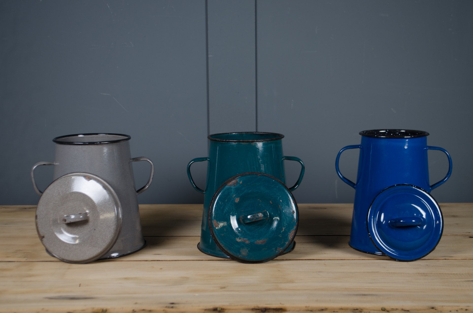 
enamel canisters for food compost waste grey, teal, and blue on a wooden surface with a dark grey background.