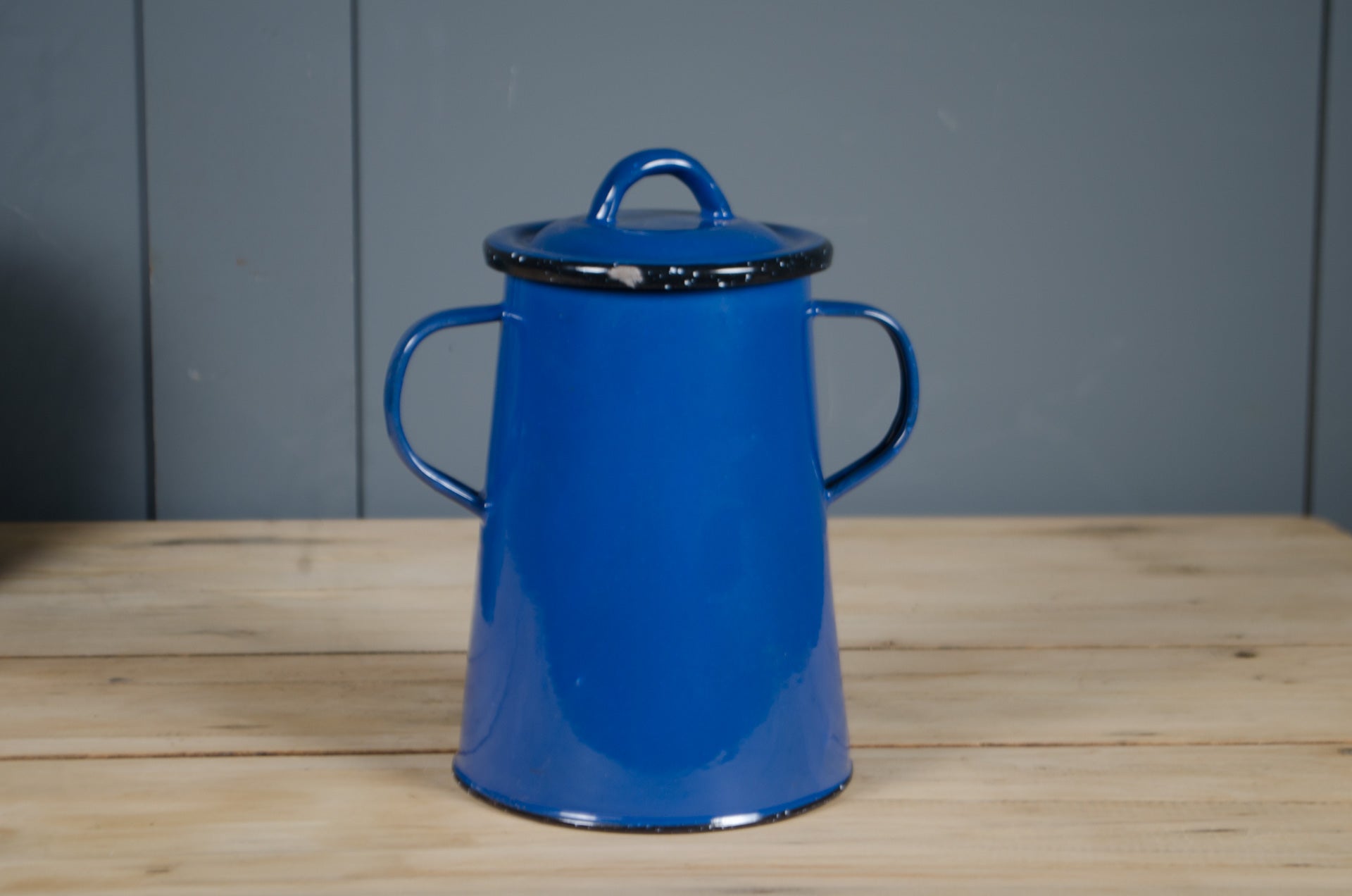
Blue enamel dog treat container with a lid on a wooden surface against a grey wall.