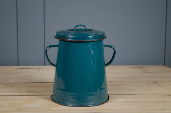 Teal metal bucket with handles on a wooden surface against a gray wall.