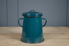 Teal metal bucket with handles on a wooden surface against a gray wall.