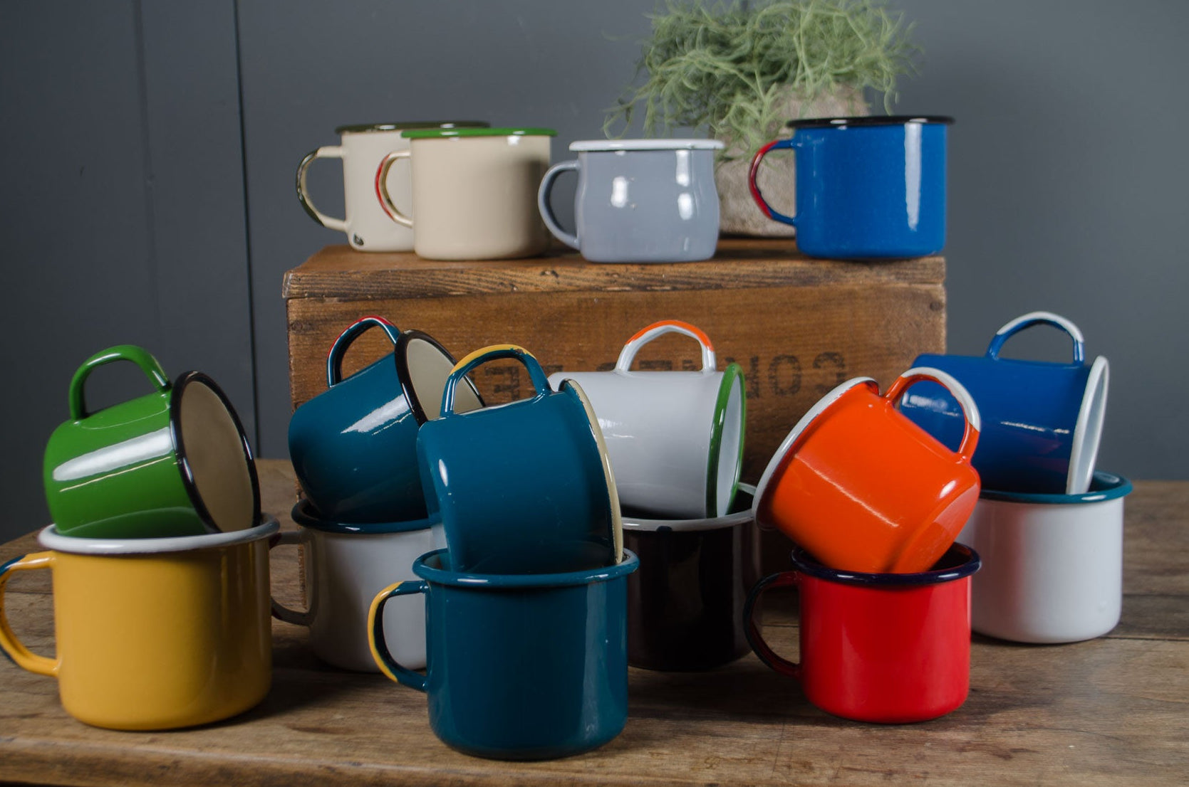 
Colorful vintage enamel mugs on a wooden table with a gray wall background